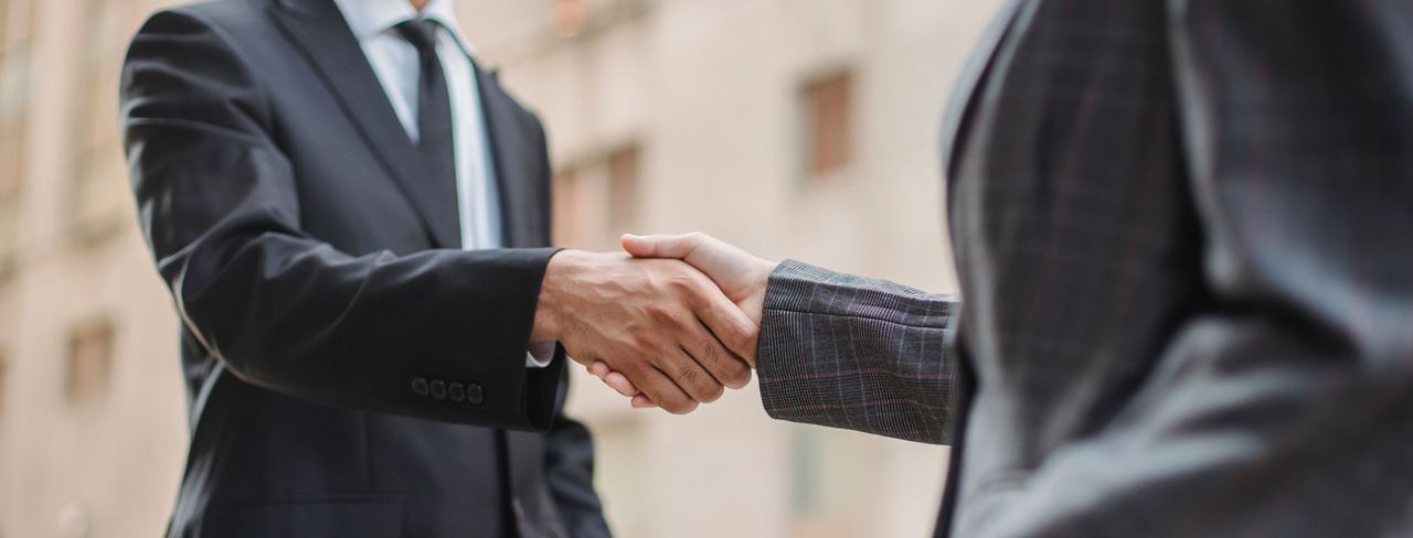 Two people in suits shaking hands outside a building