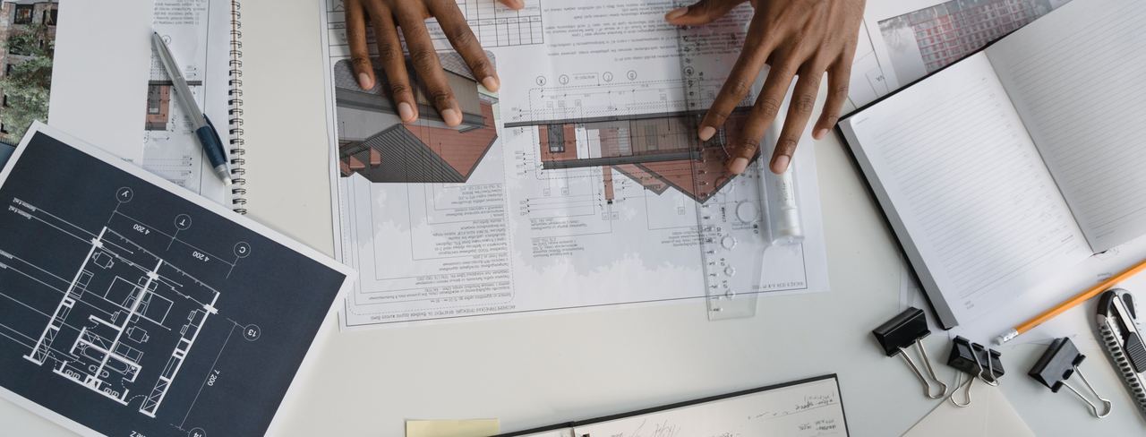 Hands reviewing drawings and paperwork spread across a desk