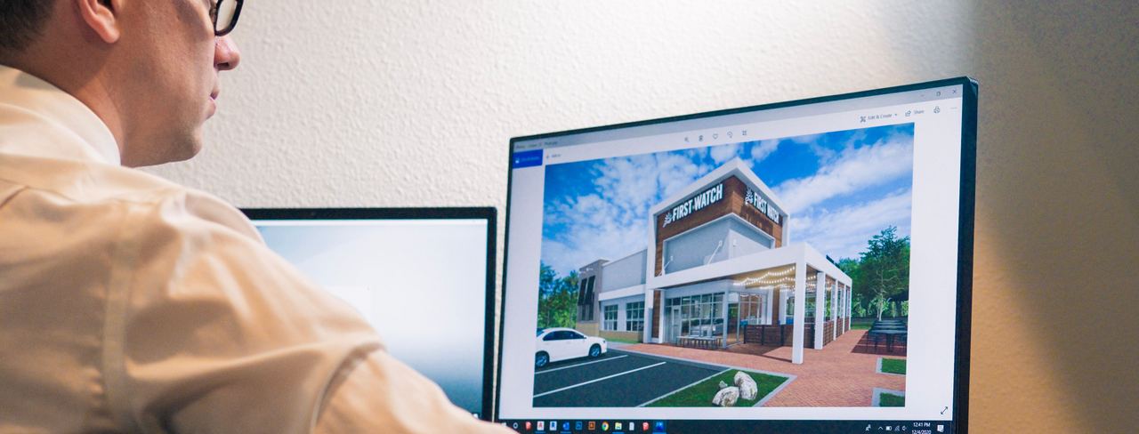 A designer at a monitor showing a 3D building model