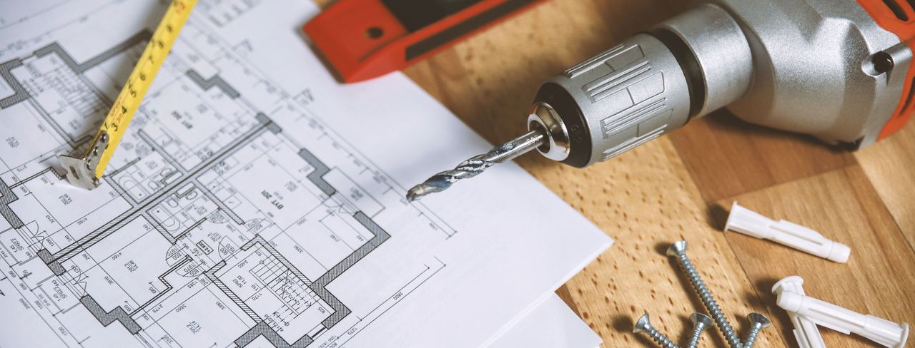 Floor plan drawings on a bench with a tape measure, level, and drill