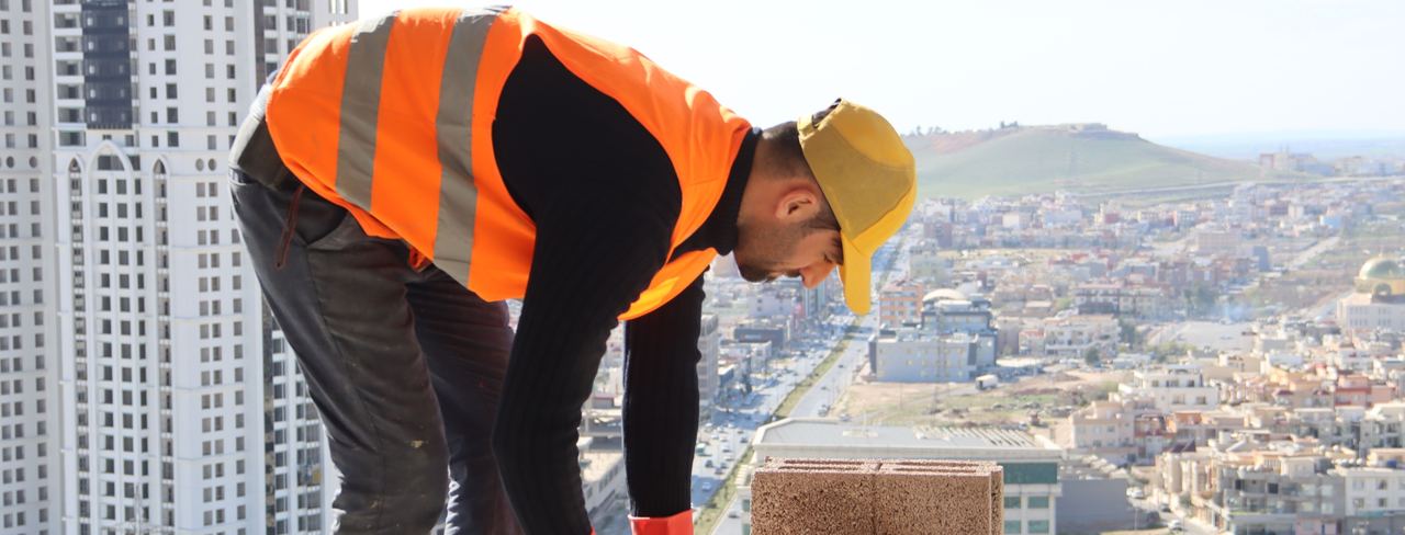 A worker laying block on a jobsite above a city skyline